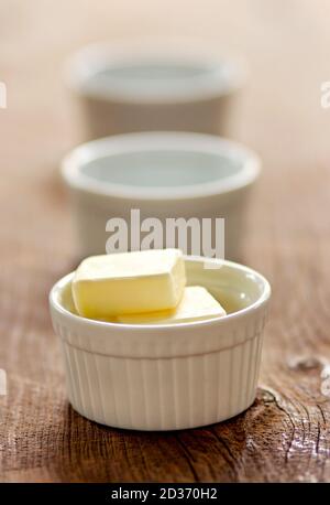 Butterwürfel in weißen Ramekins auf Holz-Tischplatte. Stockfoto