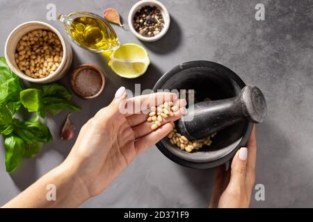 Frauenhände bereiten gesunde Pesto-Sauce in einem Mörser Stockfoto