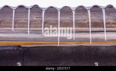 Transparente schmelzende Eiszapfen, die an warmen sonnigen Frühlingstag auf dem Holzhausdach hängen. Stockfoto