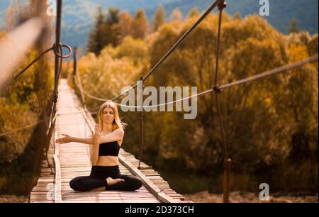 Junge Frau streckt die Arme und macht Yoga-Übungen auf der Brücke Über dem Fluss Stockfoto