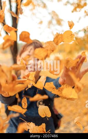 Glückliches Kind, das im Herbst im Wald mit Blättern spielt. Mädchen werfen trockene Blätter in die Kamera.Saisonale Outdoor-Aktivitäten mit Kindern. Erfassen Stockfoto
