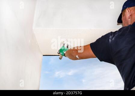Ein Bauarbeiter trägt und verwischt eine weiße Schicht Silikonputz auf die Fassaden des Hauses. Stockfoto