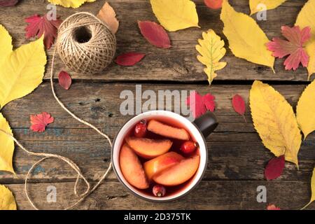 Tasse mit heißem Tee mit Obst und Hagebutten auf einem natürlichen Holzhintergrund mit Herbstblättern. Stockfoto