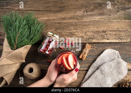 Weihnachtlicher Hintergrund mit einem Strauß Tannenzweigen und einem Glas Glühwein in Frauenhand auf einem hölzernen Hintergrund. Stockfoto