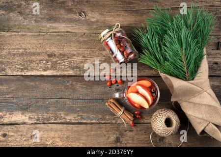 Weihnachts-Geschenkset: Ein Bouquet mit Kiefernzweigen, ein Glas Glühwein mit Zimt und Beeren auf einem Holzhintergrund. Stockfoto