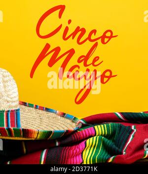 Mexikanische Serape Decke und Sombrero auf gelbem Hintergrund mit Cinco de Mayo. Stockfoto