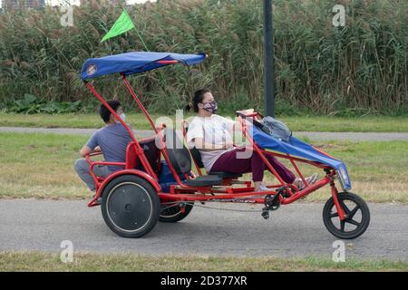 Eine asiatisch-amerikanische Mutter und Sohn mit Masken auf einem Rad Spaß 3 Rad surrey Zyklus in Flushing Meadows Corona Park in Queens, New York City. Stockfoto