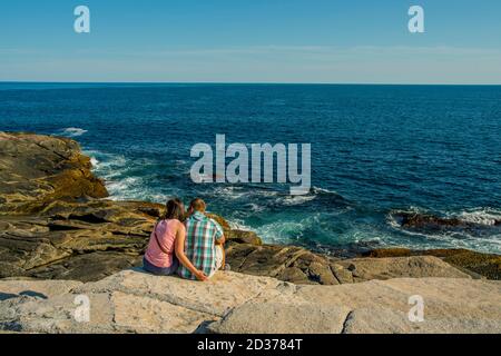 Menschen sitzen auf Granitfelsen entlang der Küste im Fischerdorf Peggy's Cove in der Nähe von Halifax, Nova Scotia, Kanada. Stockfoto