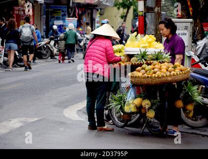 Vietnamesische Frau Kommissionierung aus, welche Früchte von der zu kaufen Straßenverkäufer in der Altstadt von Hanoi In Vietnam Stockfoto