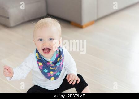 Schön gekleidet und glücklich Baby Mädchen mit blauen Augen auf dem Boden sitzen. Stockfoto