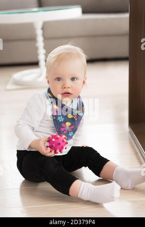 Schön gekleidet und glücklich Baby Mädchen mit blauen Augen auf dem Boden sitzen und spielen mit Ball. Stockfoto