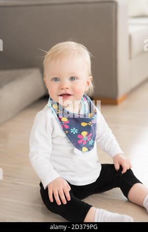 Schön gekleidet und glücklich Baby Mädchen mit blauen Augen auf dem Boden sitzen. Stockfoto