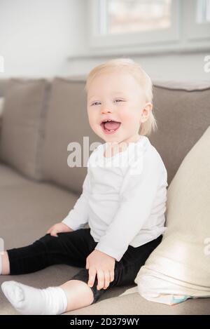 Schön gekleidet und glücklich Baby Mädchen mit blauen Augen auf dem Sofa sitzen. Stockfoto