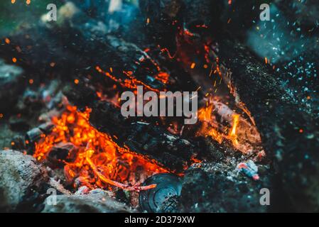Lebhaft schwelte Feuerhölzer, die in der Nahaufnahme des Feuers verbrannt wurden. Atmosphärischer Hintergrund mit oranger Flamme des Lagerfeuers. Vollbildbild von Lagerfeuer mit Funken in bok Stockfoto