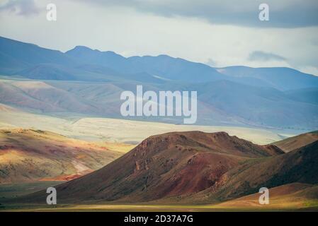 Fantasie weitläufige Landschaft mit lebhaften mehrfarbigen Bergen im Sonnenlicht. Magentafarbener felsiger Hügel im malerischen Bergtal. Bunte sonnige Landschaft mit Multi-CO Stockfoto