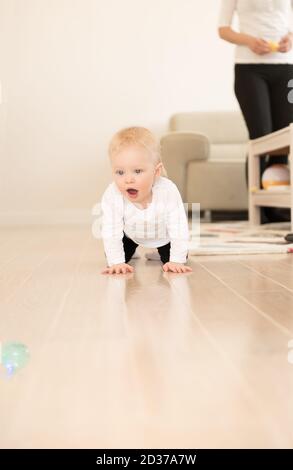 Schön gekleidet und glücklich Baby Mädchen mit blauen Augen kriechen auf dem Boden. Spielen mit Ball. Stockfoto