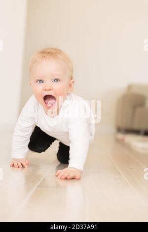 Schön gekleidet und glücklich Baby Mädchen mit blauen Augen kriechen auf dem Boden. Stockfoto