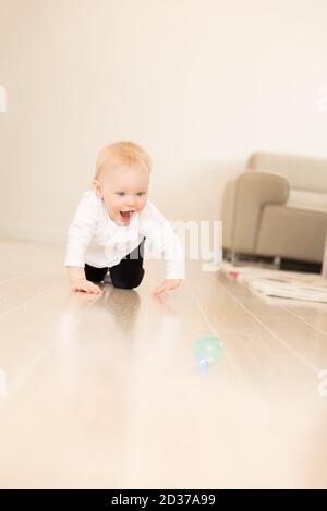 Schön gekleidet und glücklich Baby Mädchen mit blauen Augen kriechen auf dem Boden. Spielen mit Ball. Stockfoto