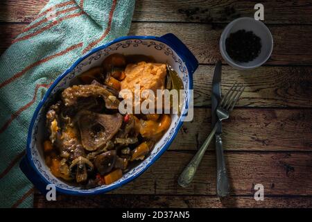 Ossobuco in Kochsauce mit Karotte, Zwiebel, Paprika und Pilzen, begleitet von Süßkartoffelpüree in einer Vintage-Platte, in Overhead-Ansicht auf einem Stockfoto