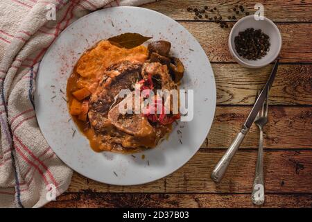 Ossobuco in Kochsauce mit Karotte, Zwiebel, Paprika und Pilzen, begleitet von Süßkartoffelpüree auf einem weißen Teller, in der Ansicht von oben auf einem ru Stockfoto