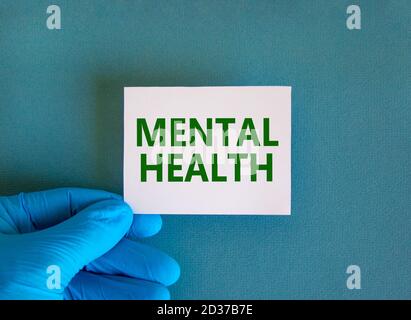 Hand in blauem Handschuh mit weißer Karte. Begriff „mentale Gesundheit“. Medizinisches und psychologisches Konzept. Kopierbereich, schöner blauer Hintergrund. Stockfoto