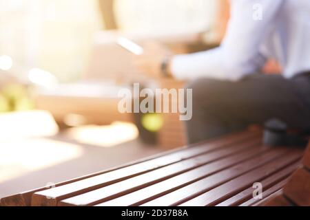 Mann mit Smartphone und lächeln, während im Freien sitzen, konzentrieren sich auf Holzbank Stockfoto