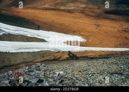 Schöner kleiner Gletscher im steinigen Bergtal mit Schmelzwasser und Moosen. Schmelzwasser fließt von Gletscherzunge hinter Steinen mit Flechten. Malerische Alp Stockfoto