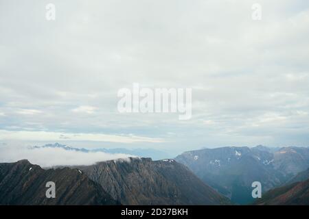 Atmosphärische minimalistische alpine Landschaft mit großen rockies und riesigen schneebedeckten Bergen. Niedrige Wolke über schönen felsigen Grat. Wundervolles ruhiges Hochland Stockfoto