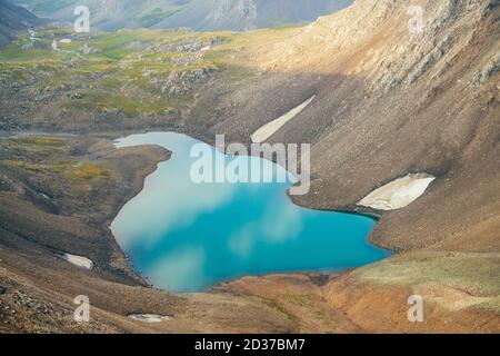 Atmosphärische minimalistische alpine Landschaft mit schönen Gletschersee im Hochland Tal zwischen felsigen Bergen. Schneestücke rund um den Bergsee amon Stockfoto