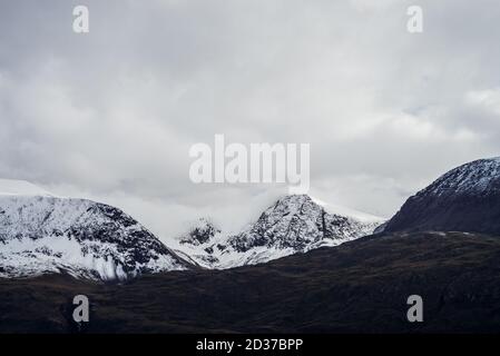 Große schwarze Berge mit weißem Schnee auf Gipfeln und Gletschern. Dramatische Landschaft mit verschneiten Bergen unter wolkig grauem Himmel. Stimmungsvolle alpine Landschaft Stockfoto