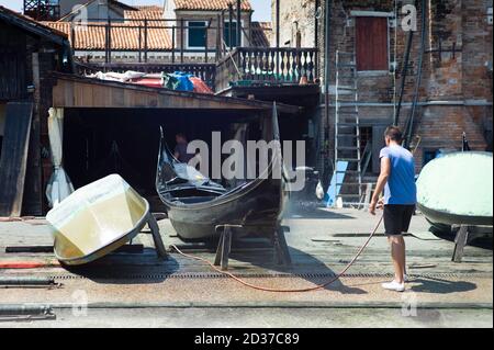 Mann im Hemd, der die Außenseite einer schwarzen Gondel putzt Auf einer Gondel Reparaturwerft in der Nähe des Canale Grande in Venedig Stockfoto