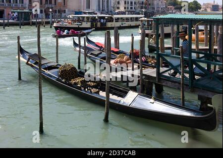 Drei reich verzierte Gondeln sind zwischen Holzpfosten in einem Wasserkanal in Venedig, Italien, angedockt. Der Gondoliere wartet auf die Kunden Stockfoto