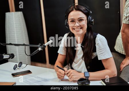 Porträt einer glücklichen jungen Radiomoderatorin, die vor der Kamera lächelt Während der Übertragung im Studio Stockfoto