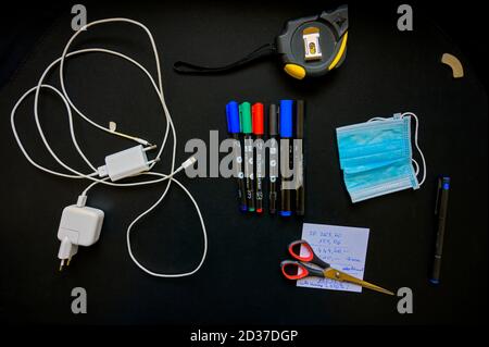 Einige Büroeinrichtungen und Mund-Nase-Maske auf einem schwarzen Schreibtisch Platte Stockfoto