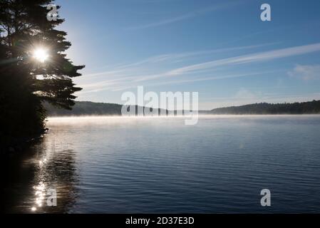 Sonnenaufgang auf einem See im Norden von Ontario. Blauer Himmel, ruhiges Wasser an einer Uferlinie mit Bäumen Stockfoto