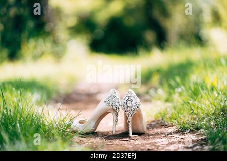 Weiße Schuhe mit einem Hintergrund mit Steinen auf einem Hintergrund von grünem Gras mit einer flachen Tiefe des Feldes verziert. Stockfoto