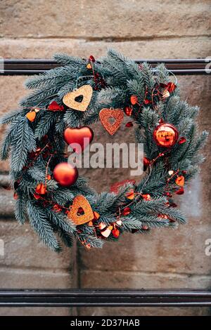 Weihnachtskranz aus Tannenzweigen mit roten Weihnachtsdekorationen an einer Steinwand. Stockfoto