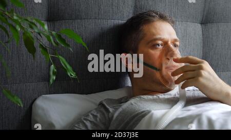 Kranker Mann mit Inhalatormaske auf dem Gesicht im Bett. Konzept zur Vorbeugung von Coronavirus. Stockfoto