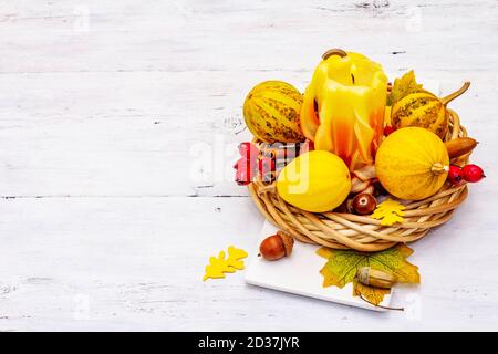 Herbstkomposition für Thanksgiving oder Halloween. Brennende geschnitzte Kerze, reife Kürbisse, Eicheln, Herbstblätter und Hagebutten. Weiße Holzbretter b Stockfoto