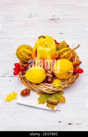 Herbstkomposition für Thanksgiving oder Halloween. Brennende geschnitzte Kerze, reife Kürbisse, Eicheln, Herbstblätter und Hagebutten. Weiße Holzbretter b Stockfoto
