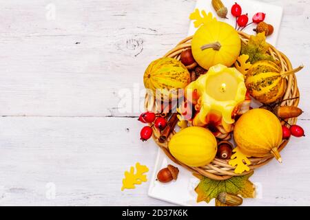 Herbstkomposition für Thanksgiving oder Halloween. Brennende geschnitzte Kerze, reife Kürbisse, Eicheln, Herbstblätter und Hagebutten. Weiße Holzbretter b Stockfoto