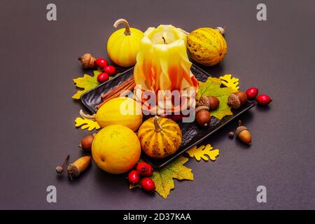 Herbstkomposition für Thanksgiving oder Halloween. Brennende geschnitzte Kerze, reife Kürbisse, Eicheln, Herbstblätter und Hagebutten. Steinbeton hintergr Stockfoto