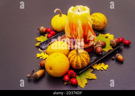 Herbstkomposition für Thanksgiving oder Halloween. Brennende geschnitzte Kerze, reife Kürbisse, Eicheln, Herbstblätter und Hagebutten. Steinbeton hintergr Stockfoto