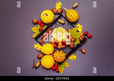 Herbstkomposition für Thanksgiving oder Halloween. Brennende geschnitzte Kerze, reife Kürbisse, Eicheln, Herbstblätter und Hagebutten. Steinbeton hintergr Stockfoto