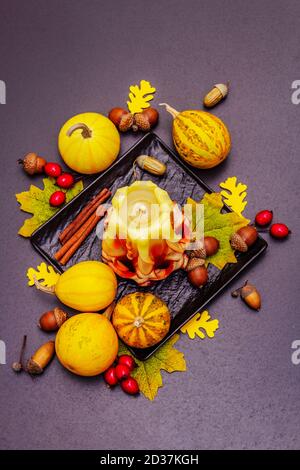 Herbstkomposition für Thanksgiving oder Halloween. Brennende geschnitzte Kerze, reife Kürbisse, Eicheln, Herbstblätter und Hagebutten. Steinbeton hintergr Stockfoto