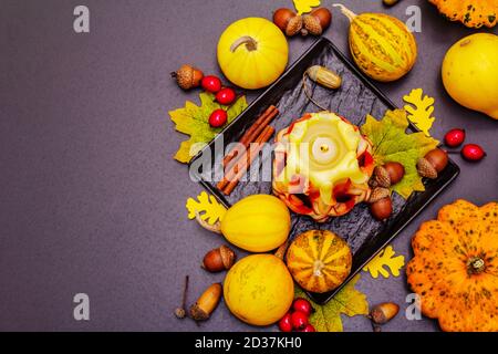 Herbstkomposition für Thanksgiving oder Halloween. Brennende geschnitzte Kerze, reife Kürbisse, Eicheln, Herbstblätter und Hagebutten. Steinbeton hintergr Stockfoto