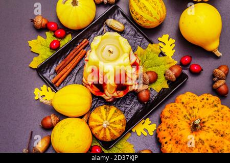 Herbstkomposition für Thanksgiving oder Halloween. Brennende geschnitzte Kerze, reife Kürbisse, Eicheln, Herbstblätter und Hagebutten. Steinbeton hintergr Stockfoto