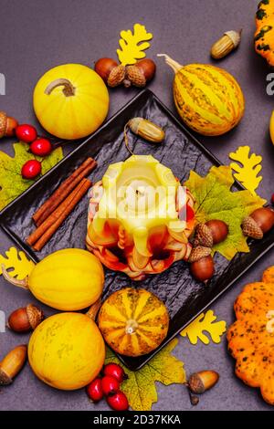 Herbstkomposition für Thanksgiving oder Halloween. Brennende geschnitzte Kerze, reife Kürbisse, Eicheln, Herbstblätter und Hagebutten. Steinbeton hintergr Stockfoto