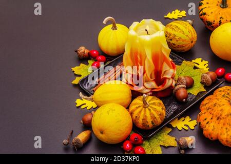 Herbstkomposition für Thanksgiving oder Halloween. Brennende geschnitzte Kerze, reife Kürbisse, Eicheln, Herbstblätter und Hagebutten. Steinbeton hintergr Stockfoto