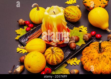 Herbstkomposition für Thanksgiving oder Halloween. Brennende geschnitzte Kerze, reife Kürbisse, Eicheln, Herbstblätter und Hagebutten. Steinbeton hintergr Stockfoto